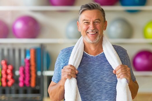 A smiling man with a towel around his neck after a workout at the gym